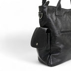 Flanc du sac noir en gros plan, poche à rabat boutonnée, anneau métallique et cuir végan froissé