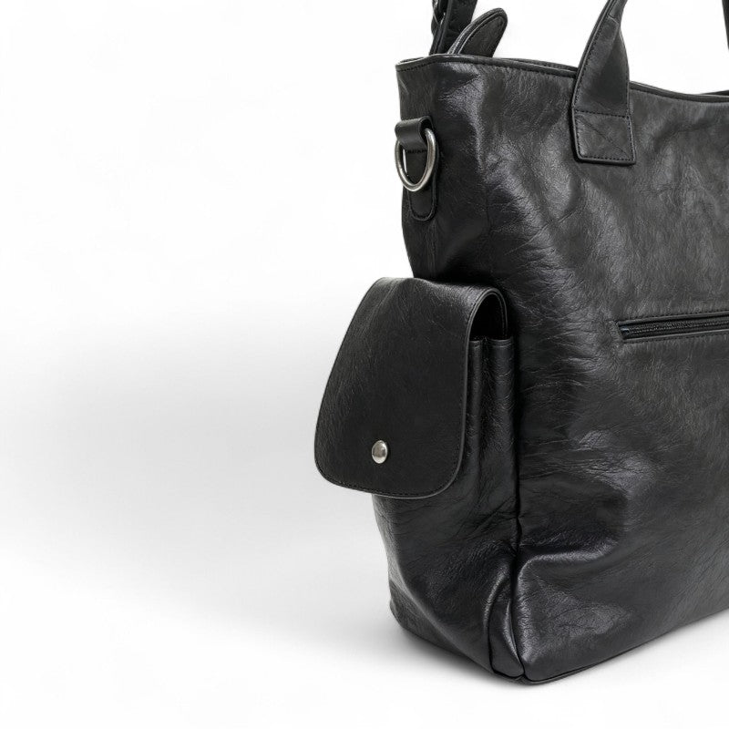 Flanc du sac noir en gros plan, poche à rabat boutonnée, anneau métallique et cuir végan froissé