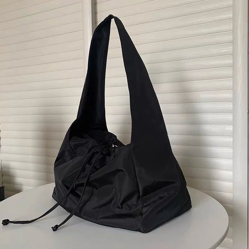 Cabas souple en nylon noir posé sur une table ronde, anse large et cordons de serrage noués