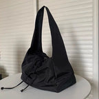Cabas souple en nylon noir posé sur une table ronde, anse large et cordons de serrage noués