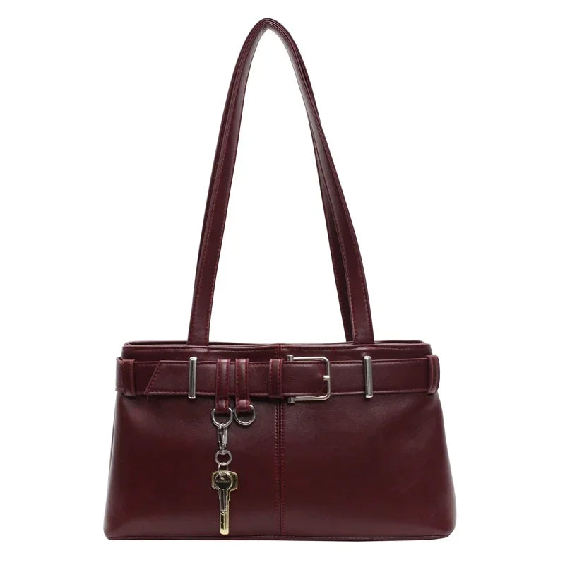 Sac d'épaule bordeaux à anse longue, présenté de face, ceinture ajustable et pendentif clé doré