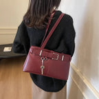 Silhouette de dos, sac bordeaux porté à l'épaule sur un pull noir, sangle en diagonale dans le dos