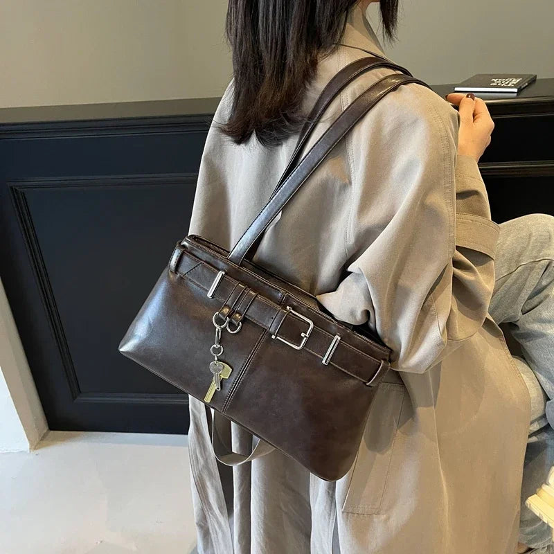 Porté à l'épaule sur un trench beige, le sac brun café tombe sous le bras, breloque clé en balancier