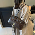 Porté à l'épaule sur un trench beige, le sac brun café tombe sous le bras, breloque clé en balancier
