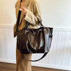 Silhouette souple du cabas brun foncé porté à l'épaule avec une veste beige, bandoulière longue