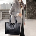 Porté à la main le long du corps, le cabas noir accompagne un manteau gris et un pantalon foncé