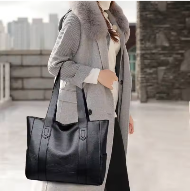 Porté à la main le long du corps, le cabas noir accompagne un manteau gris et un pantalon foncé