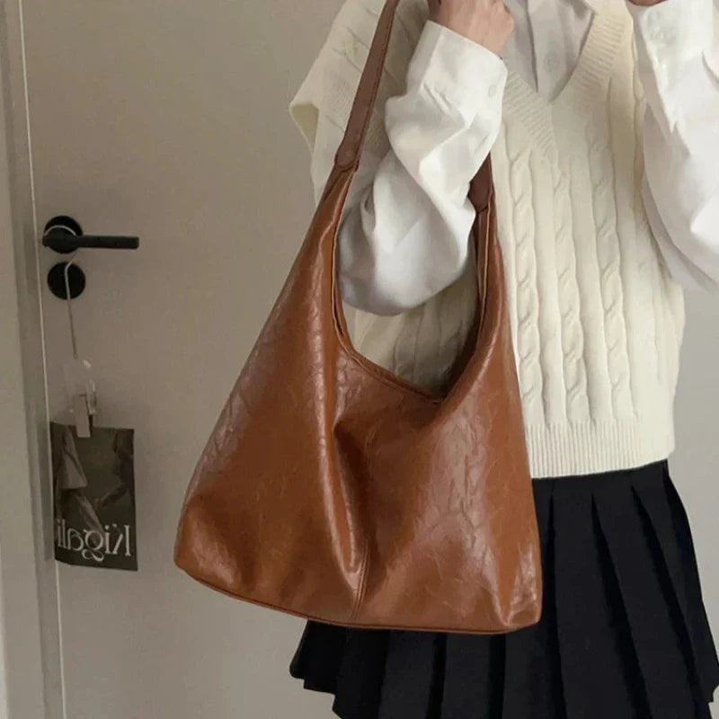 Tenue de lycéenne, gilet blanc et jupe plissée, avec le hobo cognac porté à l'épaule
