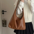 Tenue de lycéenne, gilet blanc et jupe plissée, avec le hobo cognac porté à l'épaule