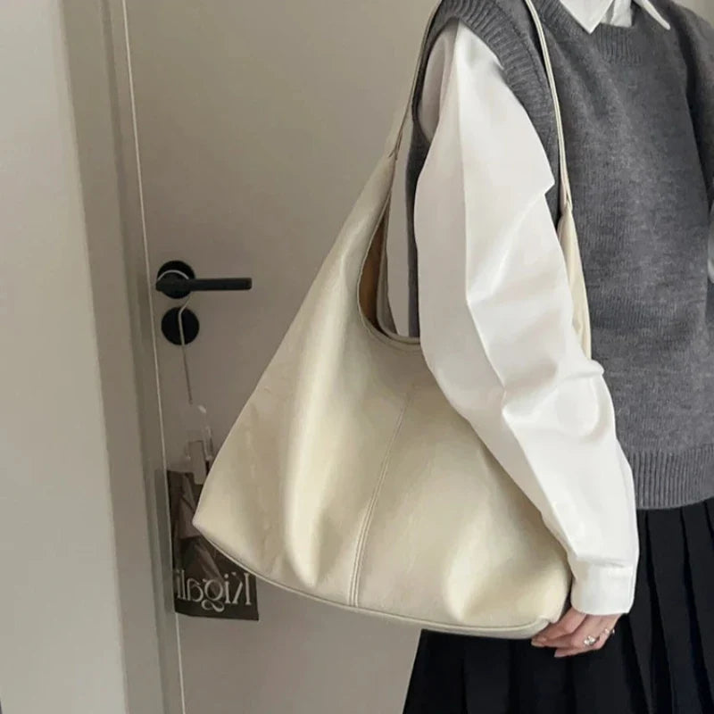 Teinte écru crème du hobo porté à l'épaule sur un débardeur gris et une chemise blanche