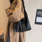 Porté à l'épaule sur un trench beige, le hobo noir s'affaisse en plis souples contre la hanche