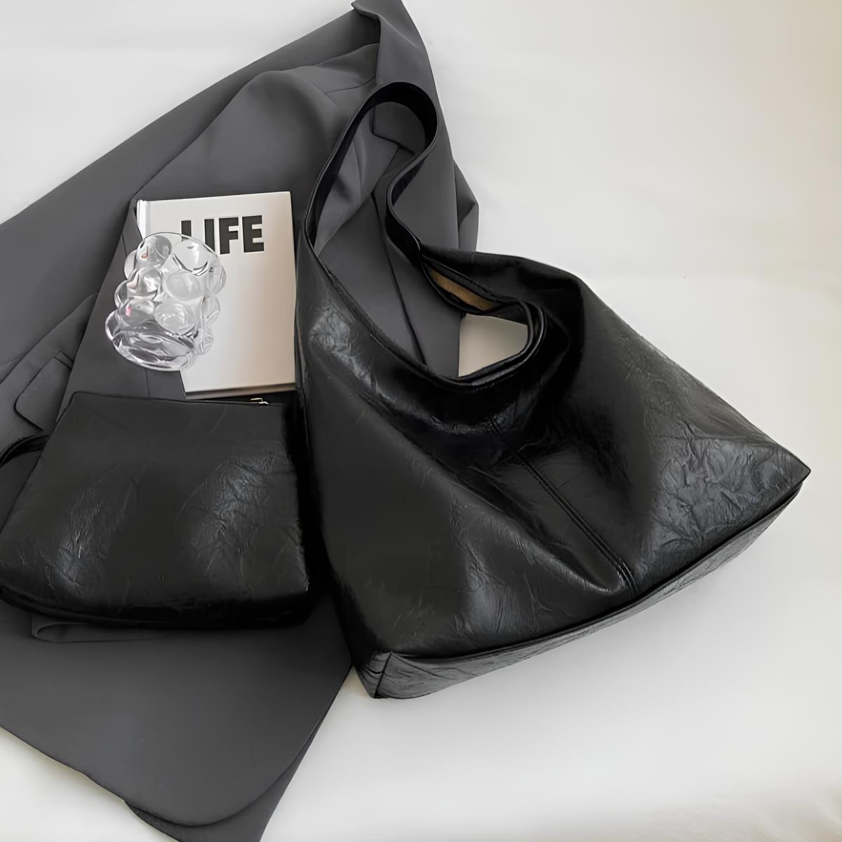 Deux sacs noirs posés à plat sur un drapé gris, près d'un livre et d'un bijou translucide