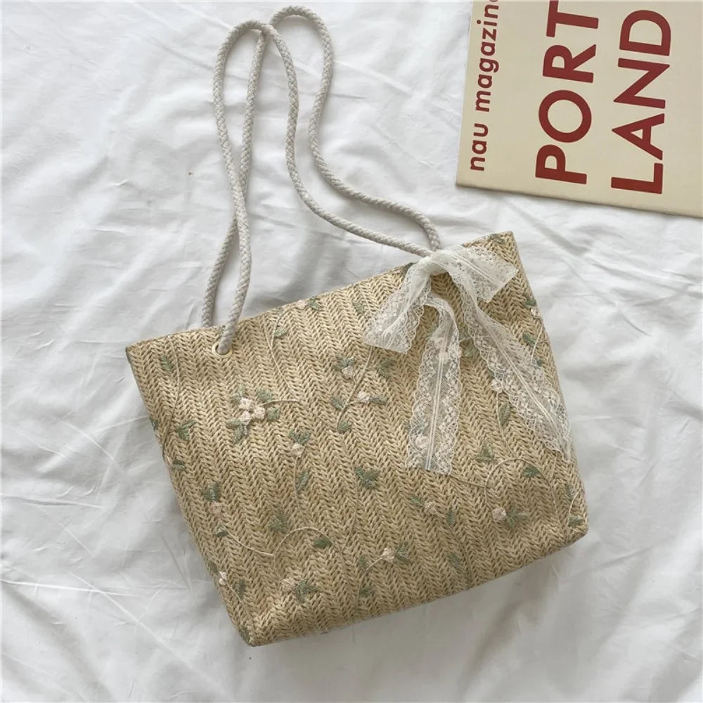 Posé à plat sur un drap froissé, cabas en paille beige semé de petites fleurs brodées vert d'eau