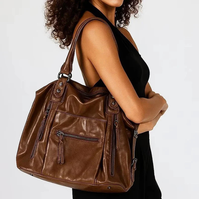 Épaulé par une femme en robe noire, le grand sac marron s'évase largement sous le bras