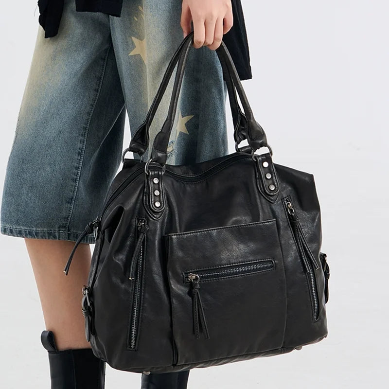 Porté à la main par une silhouette en jean clair, le grand sac noir tombe le long de la jambe