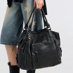 Porté à la main par une silhouette en jean clair, le grand sac noir tombe le long de la jambe