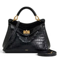 Sac à main trapèze noir effet croco, fermoir tourniquet doré et bandoulière amovible posée à côté