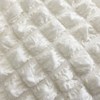 Gros plan sur le tissu gaufré à bulles écru, relief matelassé et grain souple du sac