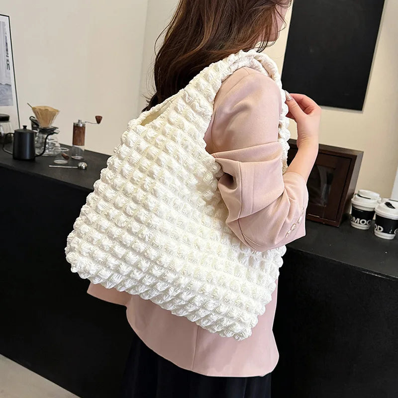 Porté à l'épaule sur un blazer rose poudré, le grand cabas écru vu de dos dans un café