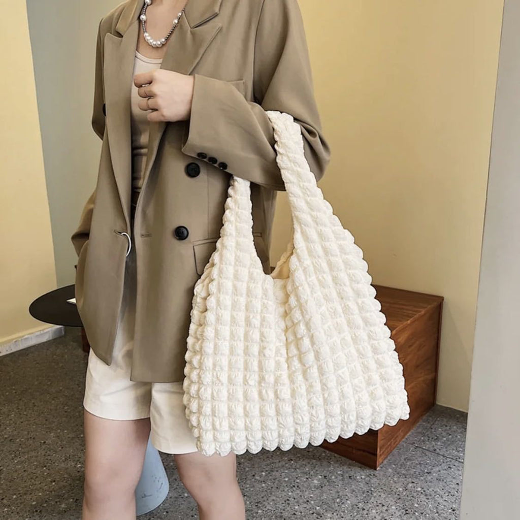 Volumineux sac écru tenu à la main devant un trench camel, tenue claire en extérieur