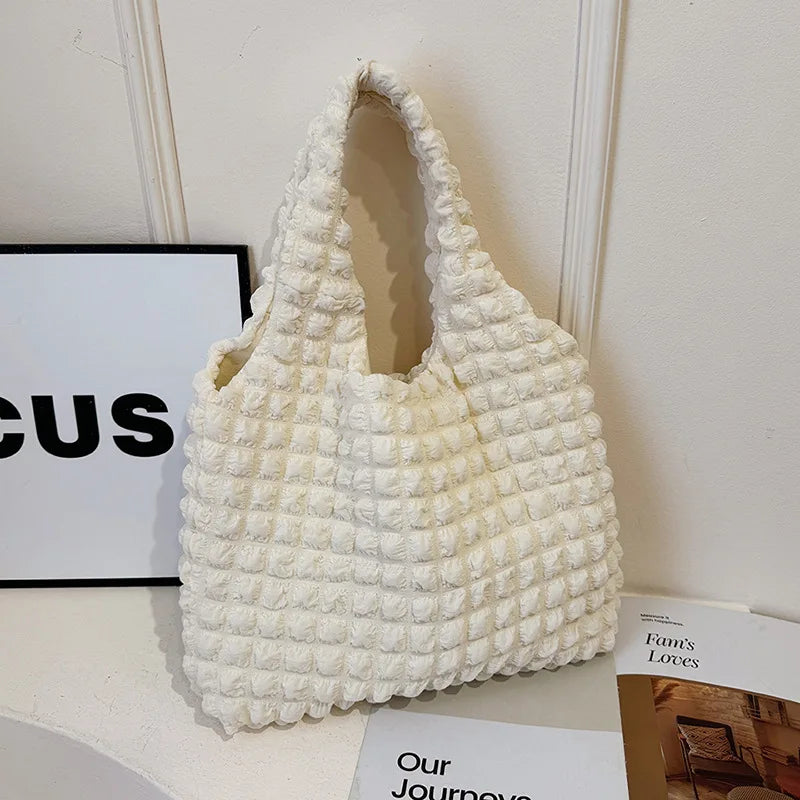 Tissu matelassé crème gonflé de bulles, sac hobo posé de trois quarts devant une affiche