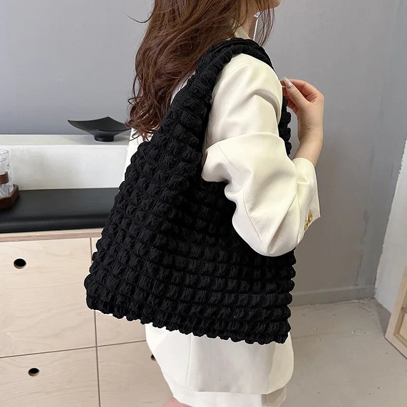 Épaule chargée du sac noir texturé, porté sur une chemise blanche dans un intérieur clair