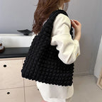 Épaule chargée du sac noir texturé, porté sur une chemise blanche dans un intérieur clair