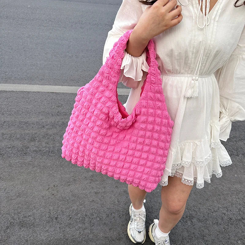 Modèle en robe blanche tenant par son anse le cabas rose vif, plan de trois quarts