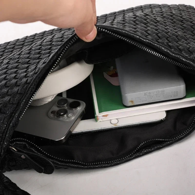 Contenu du sac noir ouvert à la main : ordinateur portable, cahier, téléphone et étui d'écouteurs