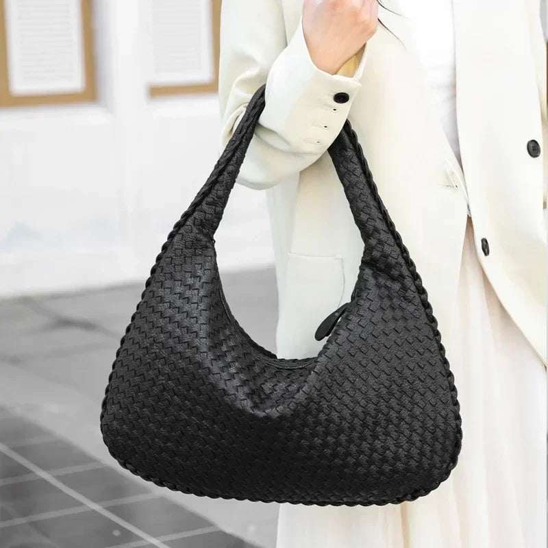 Porté à l'épaule par-dessus un manteau blanc, le hobo noir tressé retombe souplement sous le bras