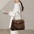 Femme en tenue blanche portant le cabas chocolat à l'épaule, une revue tenue à la main