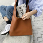 Assise sur un muret en jean et baskets, une lycéenne tient le sac caramel et un journal