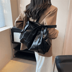 Sac noir en cuir végan porté à l'épaule sur un manteau camel, forme avachie et bien remplie