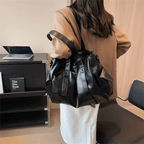 De dos dans un bureau, le grand sac noir souple repose sur l'épaule, sangle en travers