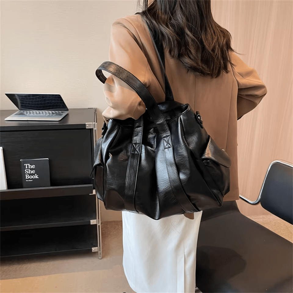 De dos dans un bureau, le grand sac noir souple repose sur l'épaule, sangle en travers