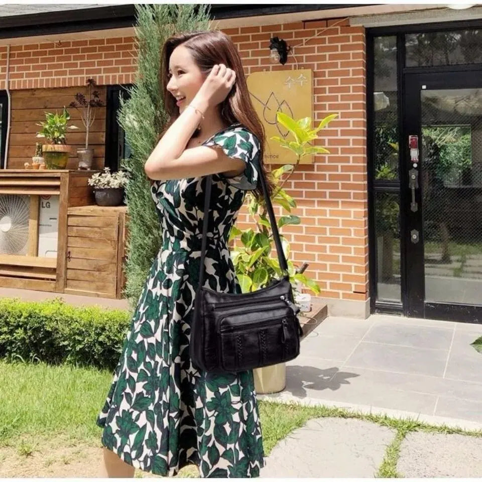 Porté en croisé sur une robe fleurie verte, le sac noir repose sur la hanche, en extérieur