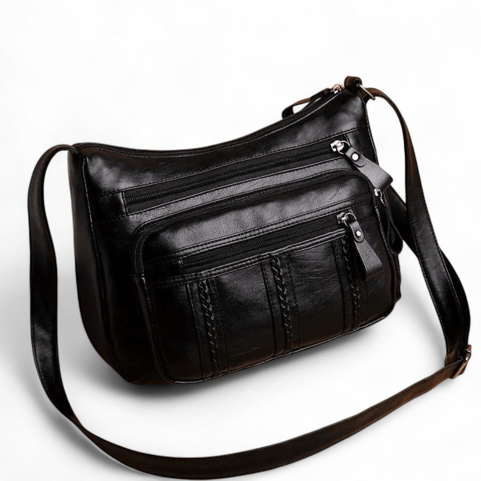 Sac noir de trois quarts, longue bandoulière réglable déployée et poches zippées latérales