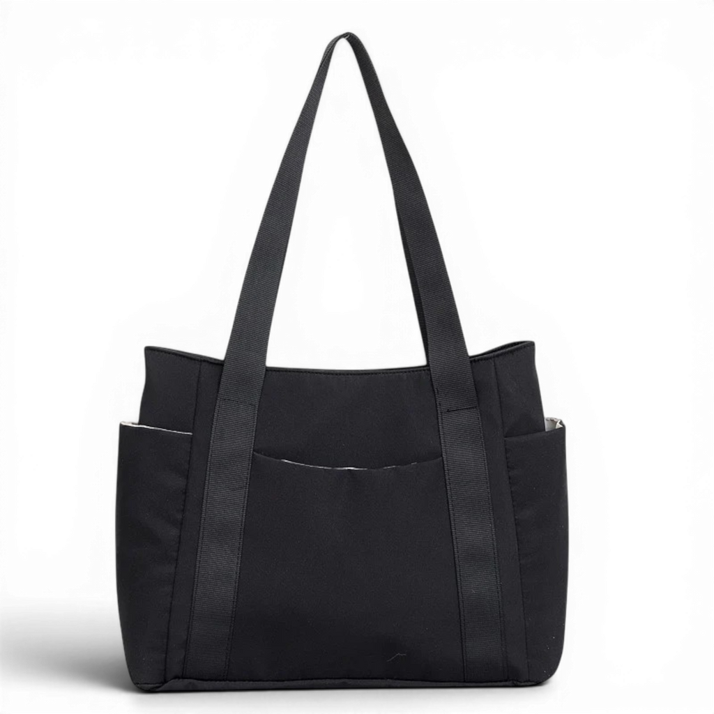 Cabas en toile de nylon noir, vu de face sur fond sombre, longues anses et poches latérales