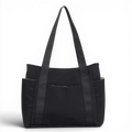 Cabas en toile de nylon noir, vu de face sur fond sombre, longues anses et poches latérales