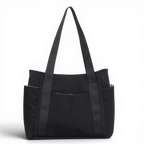 Cabas en toile de nylon noir, vu de face sur fond sombre, longues anses et poches latérales