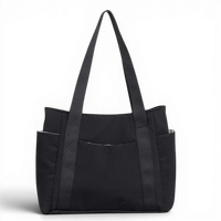 Cabas en toile de nylon noir, vu de face sur fond sombre, longues anses et poches latérales