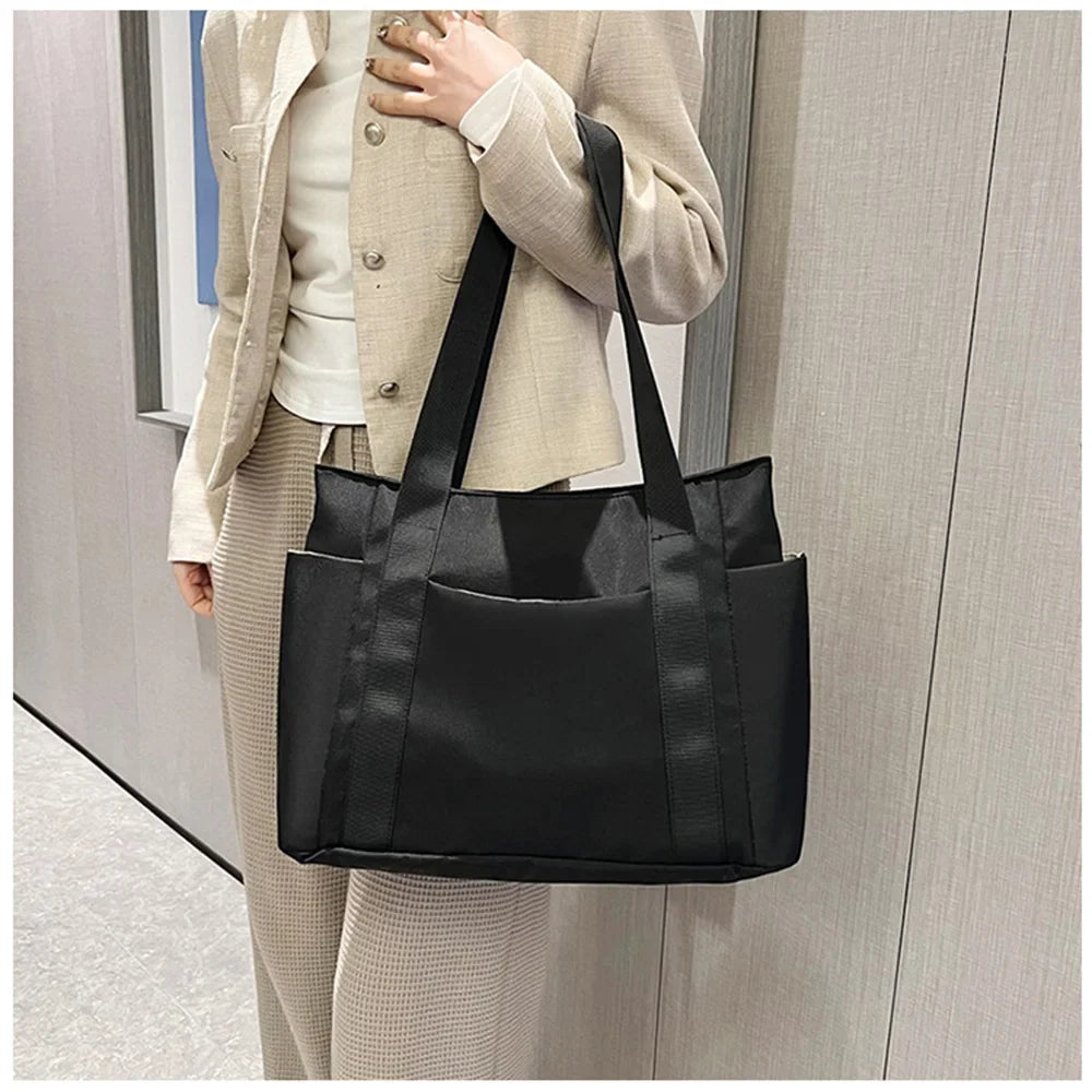 Porté à l'épaule sur un tailleur beige, le cabas noir laisse voir sa large poche plaquée