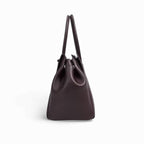 Profil étroit du sac brun aubergine, base rigide et anses rondes rassemblées vers le haut
