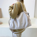 Dos d'une silhouette en veste beige portant le grand hobo blanc à l'épaule, anses tenues en main