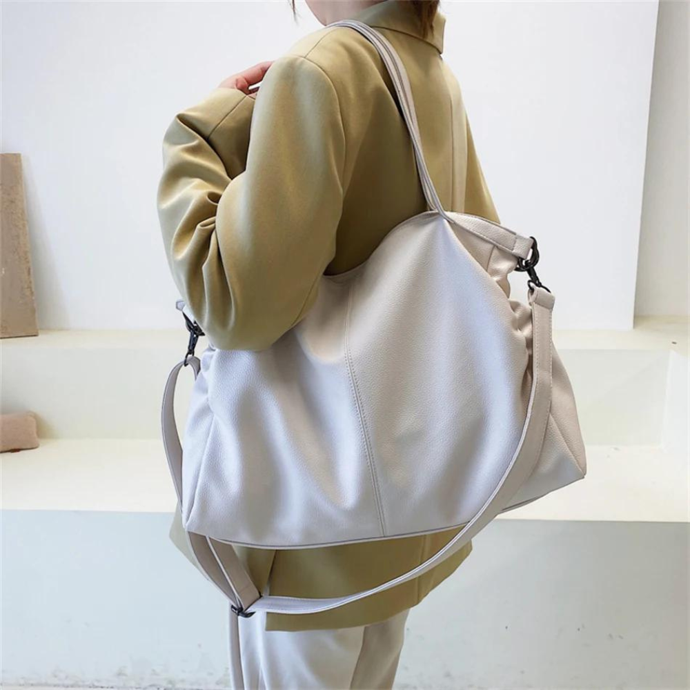 Dos d'une silhouette en veste beige portant le grand hobo blanc à l'épaule, anses tenues en main