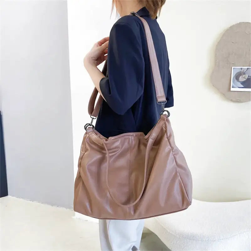 Bandoulière large sur l'épaule, le sac taupe rosé porté en croisé sur une tunique bleu marine