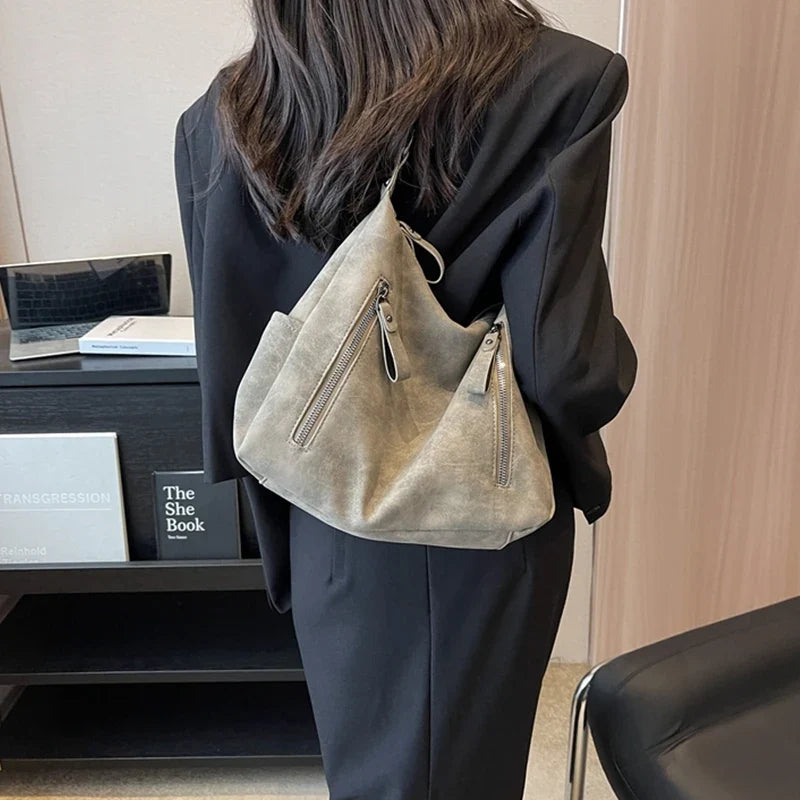 En bandoulière dans le dos sur un tailleur noir, le hobo beige grège garde sa forme souple
