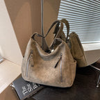 Brun taupe et souple, le sac repose sur des livres devant un store, tirettes métal apparentes