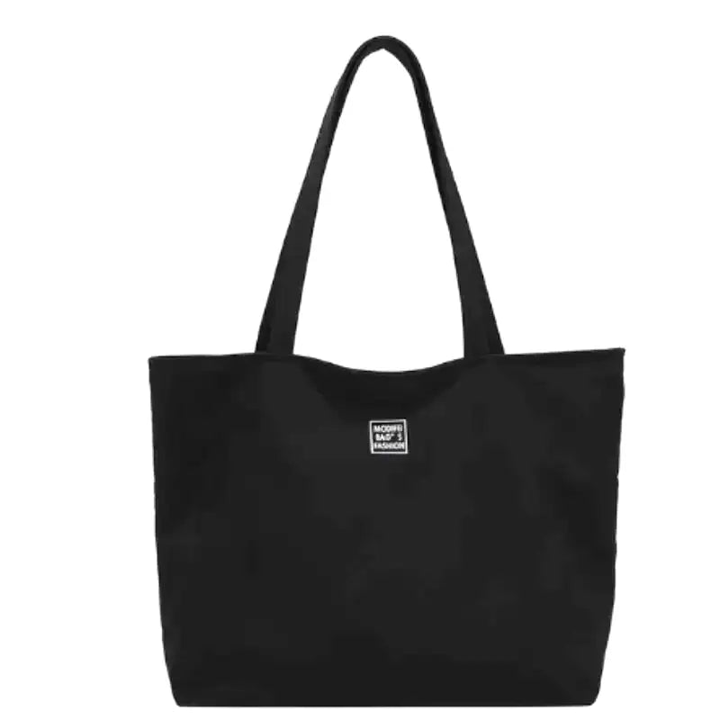 Cabas en nylon noir déperlant photographié de face, anses longues et petite étiquette sur la façade