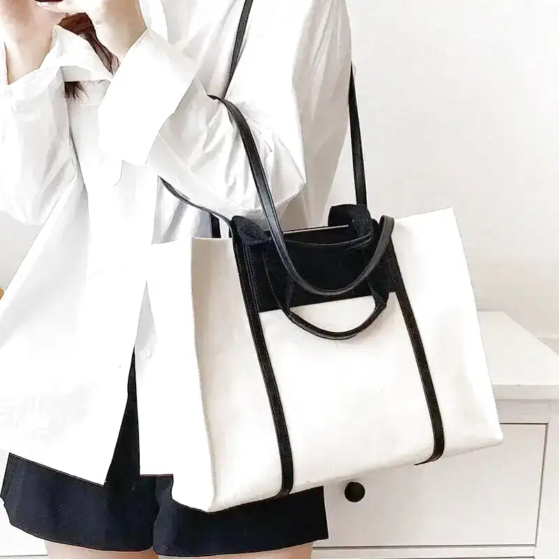 Porté à l'épaule sur une chemise blanche, grand cabas en toile blanche à bandeau et anses noirs